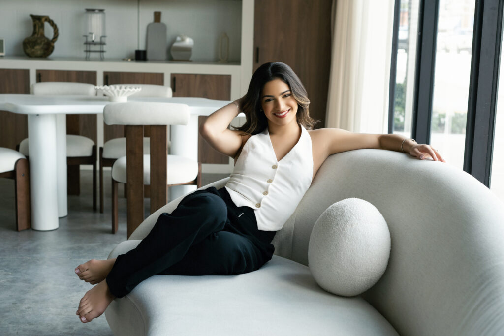 a girl sitting on a white couch smiling during a brand photoshoot.
